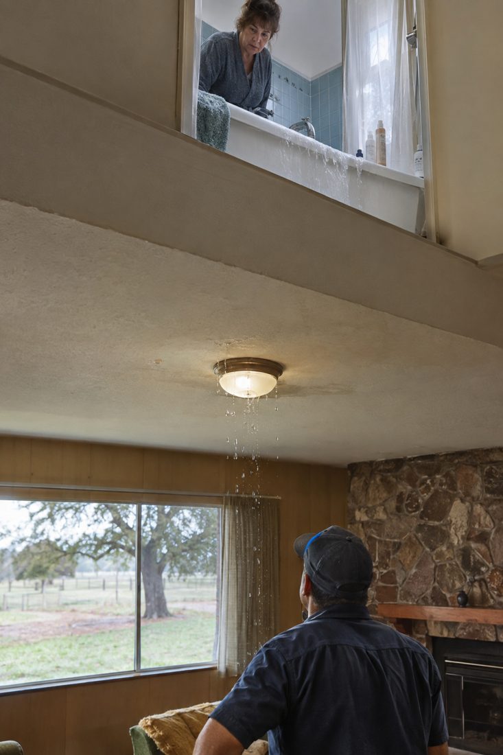 An overflowing upstairs bathtub with water dripping through the ceiling light below at a 1960s ranch house with a valley oak in California's Central Valley in Modesto, CA